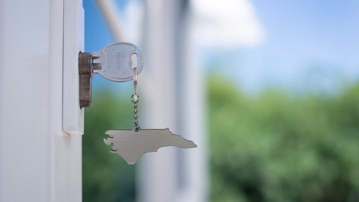 A key in a door with a keychain in the shape of North Carolina.